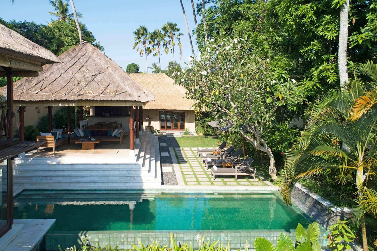 A poolside area with a thatched-roof structure, lounge chairs, and a well-maintained garden.