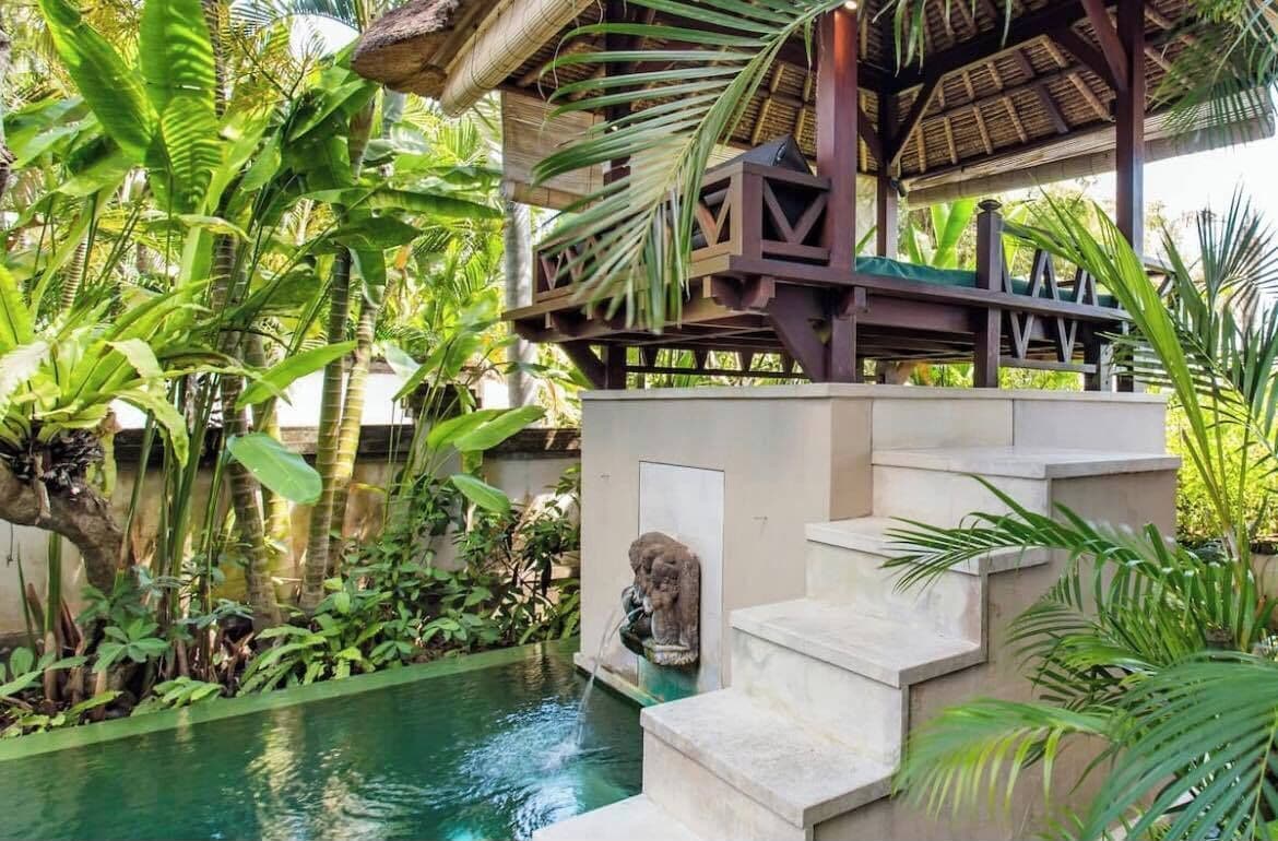 A pool area with steps leading into a water feature, surrounded by lush tropical plants.