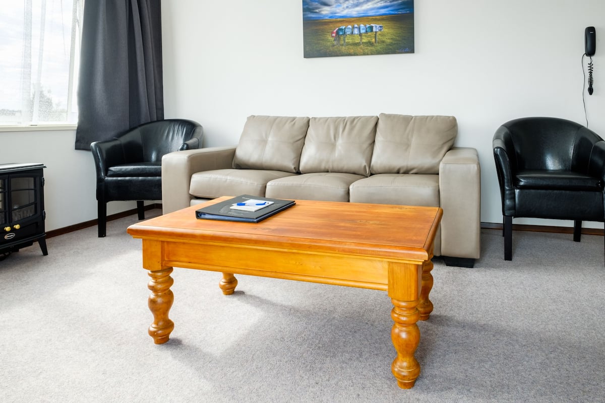 A living room with a beige sofa, two black leather chairs, a wooden coffee table, a black telephone, and a painting on the wall.