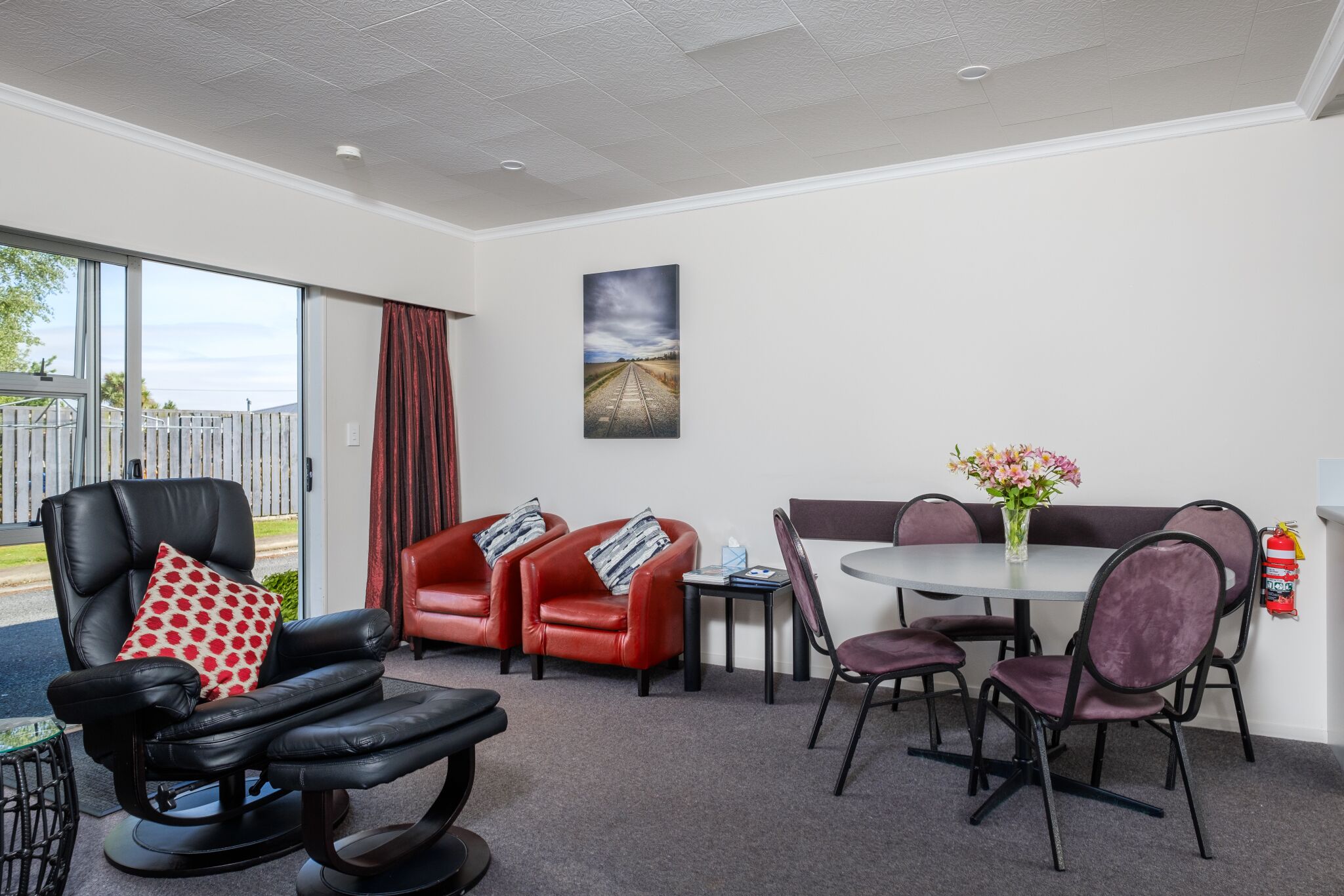 A modern room with a leather recliner, red sofas, a round dining table, and purple chairs.