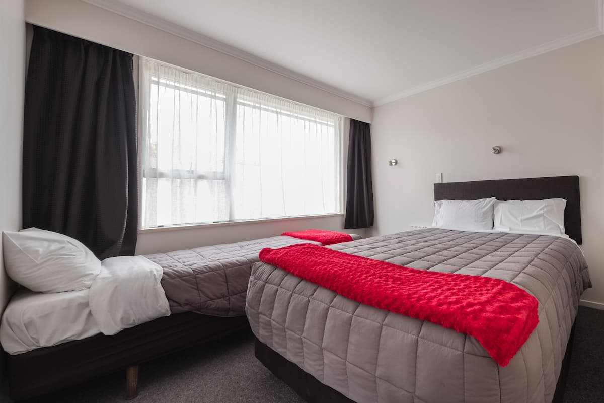 A hotel room with a large bed, a smaller bed, a window with curtains, and a red throw blanket.