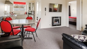 A modern living room with a fireplace, a dining area with red chairs, and a kitchen in the background.