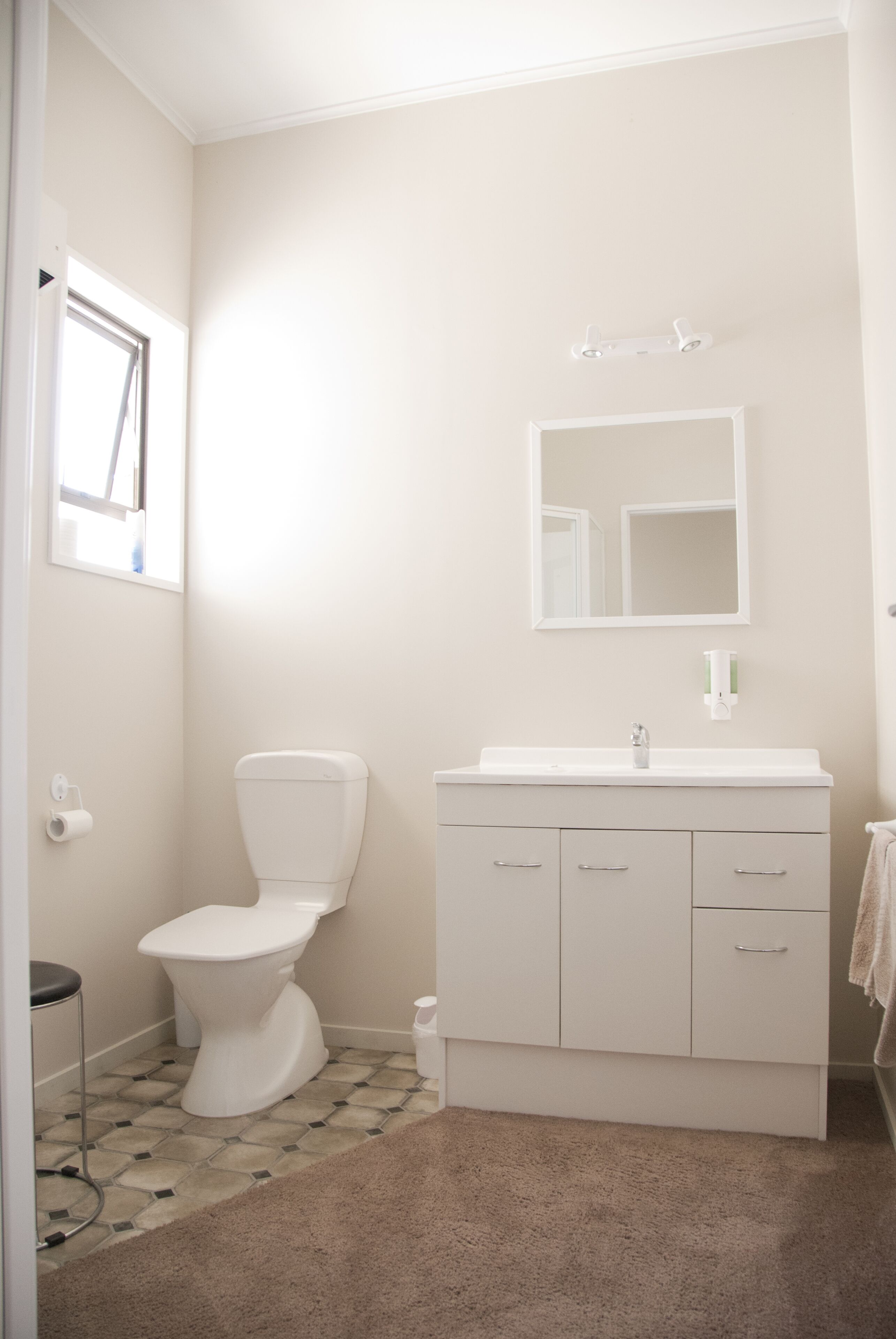 A small, clean bathroom with a toilet, sink, and mirror.