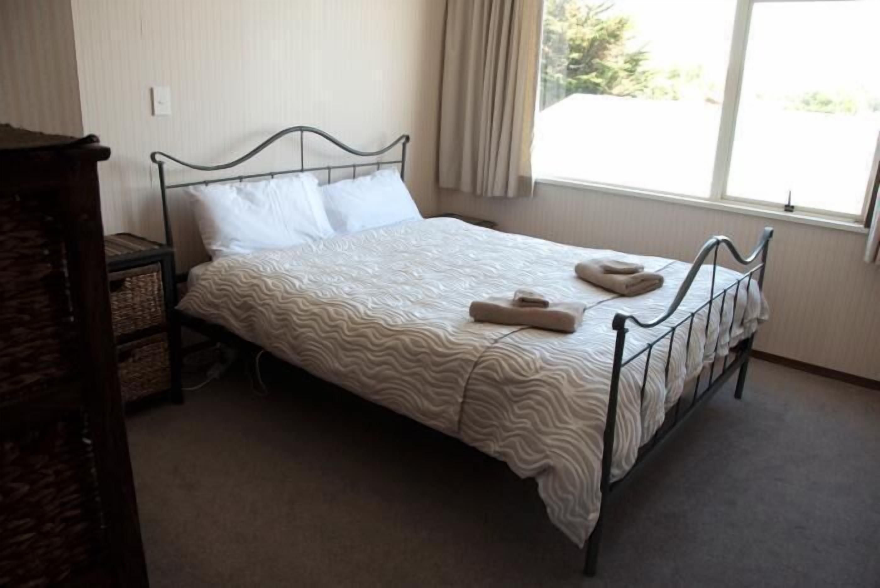 A single bed with a wavy patterned bedspread, a metal headboard, and a window with curtains.