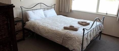A single bed with a wavy patterned bedspread, a metal headboard, and a window with curtains.