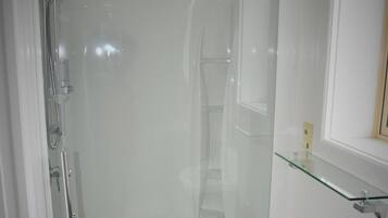 A glass-enclosed shower stall with a handheld showerhead, a glass shelf above the sink, and a black towel hanging on a rack.