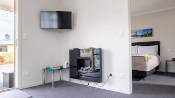 A hotel room with a bed, a TV mounted on the wall, a desk with a computer, and a small table with a chair.