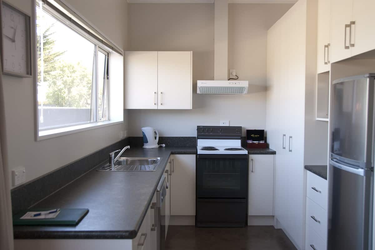 A compact kitchen with a stove, oven, and refrigerator. There is a window providing natural light and a view of trees outside.