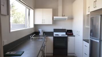 A compact kitchen with a stove, oven, and refrigerator. There is a window providing natural light and a view of trees outside.