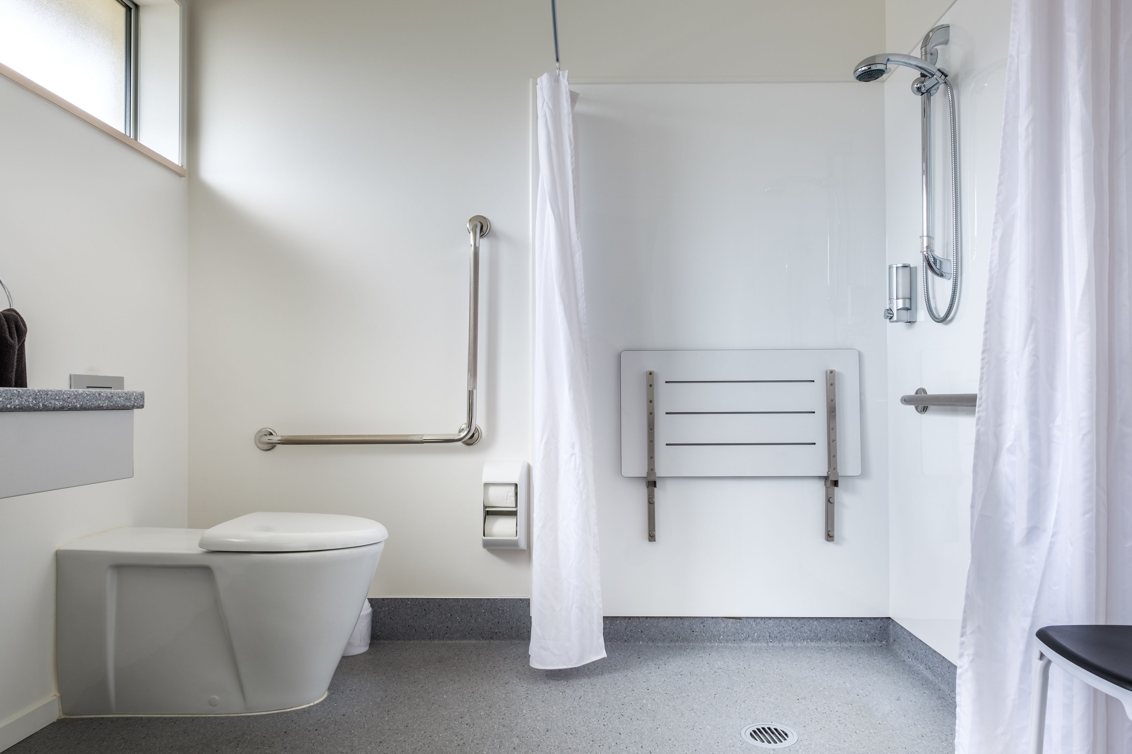 A bathroom with a toilet, grab bars, a shower, and a towel rack.