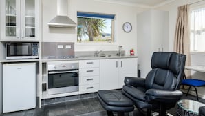A compact kitchen with white cabinets, a microwave, a built-in oven, a window with a view, and a black leather chair.