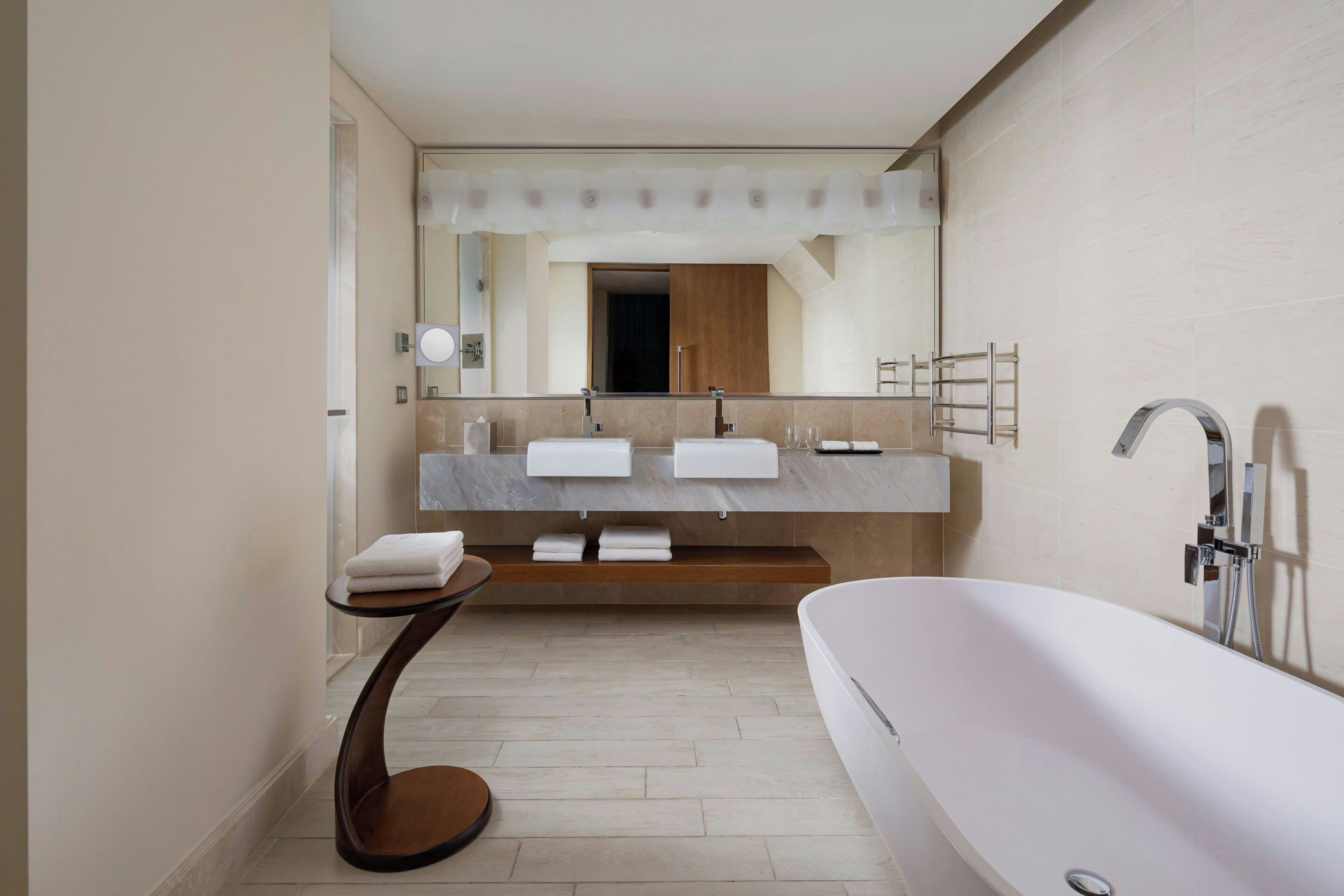 A modern bathroom with a large bathtub, two sinks, a vanity with a mirror, and a towel rack.
