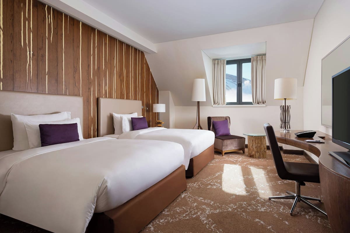 A hotel room with two beds, a desk, a chair, and a TV.