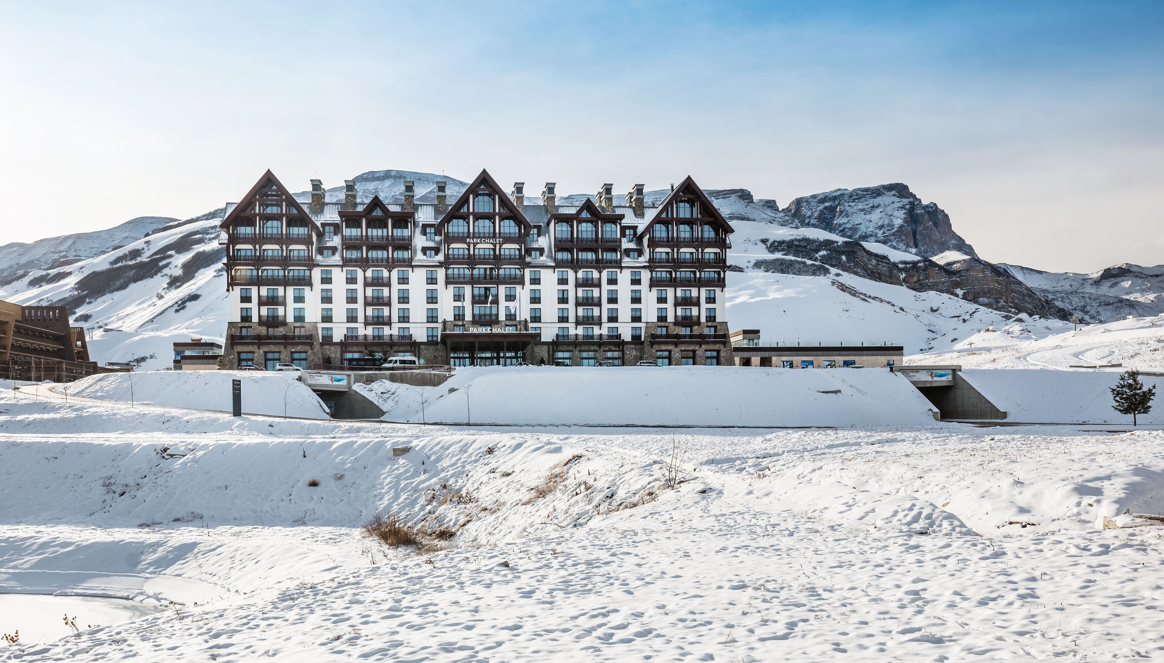 A large, multi-story hotel with a symmetrical facade, set against a backdrop of snow-covered mountains.