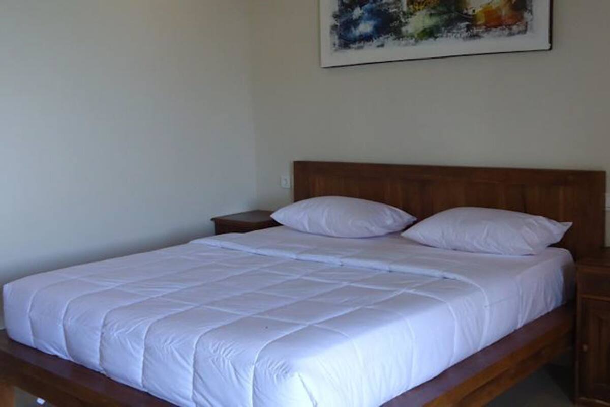 Una cama bien hecha con ropa blanca, un cabecero de madera y una mesita de noche con una lámpara.