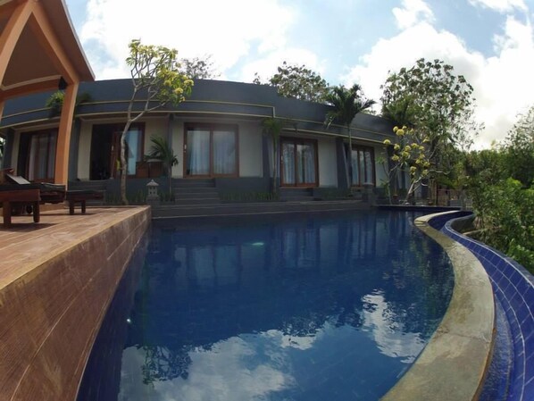 A modern building with a swimming pool, featuring a curved design and a covered patio area.