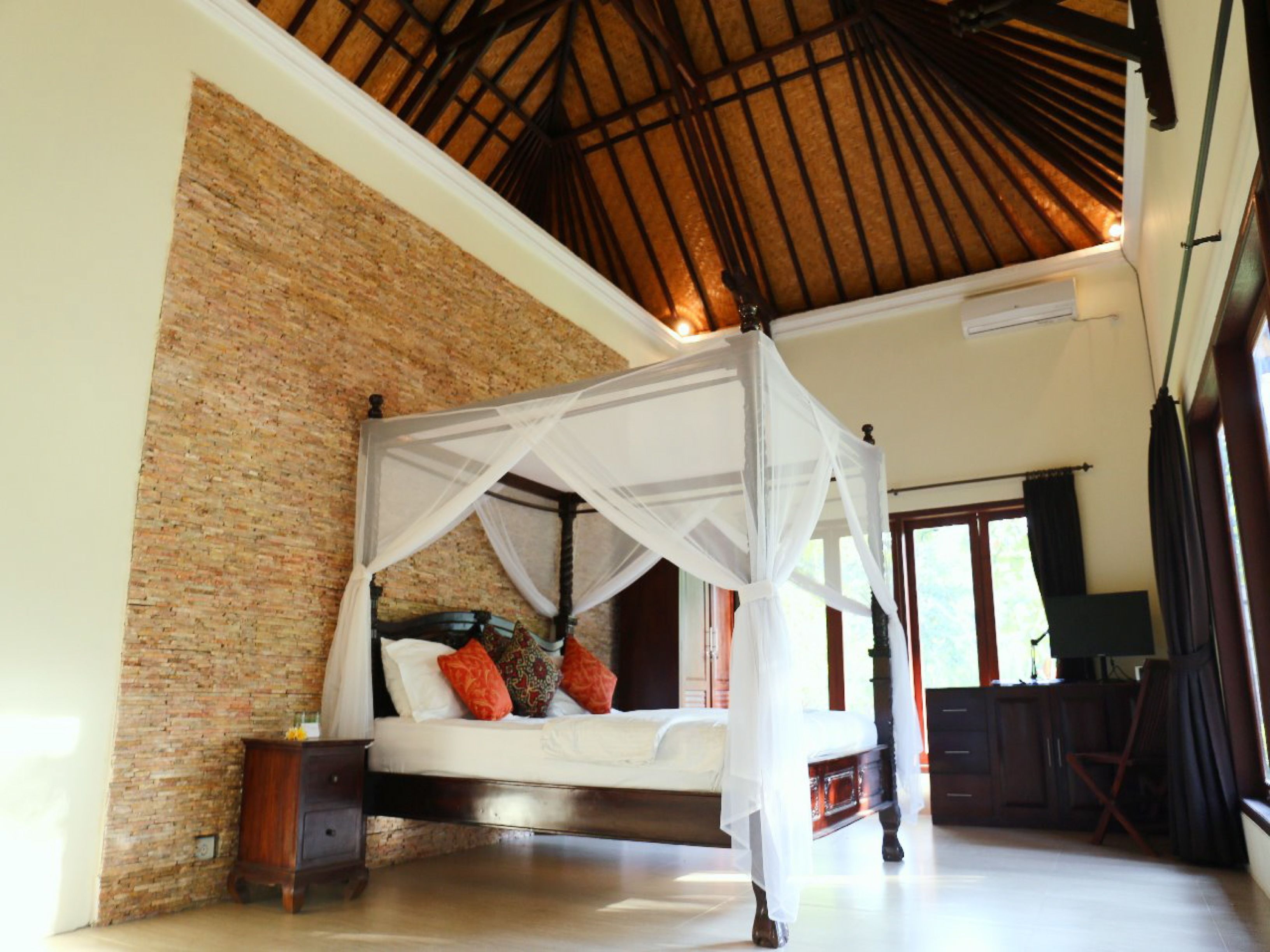 A bedroom with a four-poster bed, a brick wall, and a wooden ceiling.