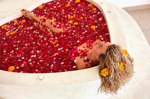 Una persona recostada en una bañera llena de pétalos rojos y amarillos.
