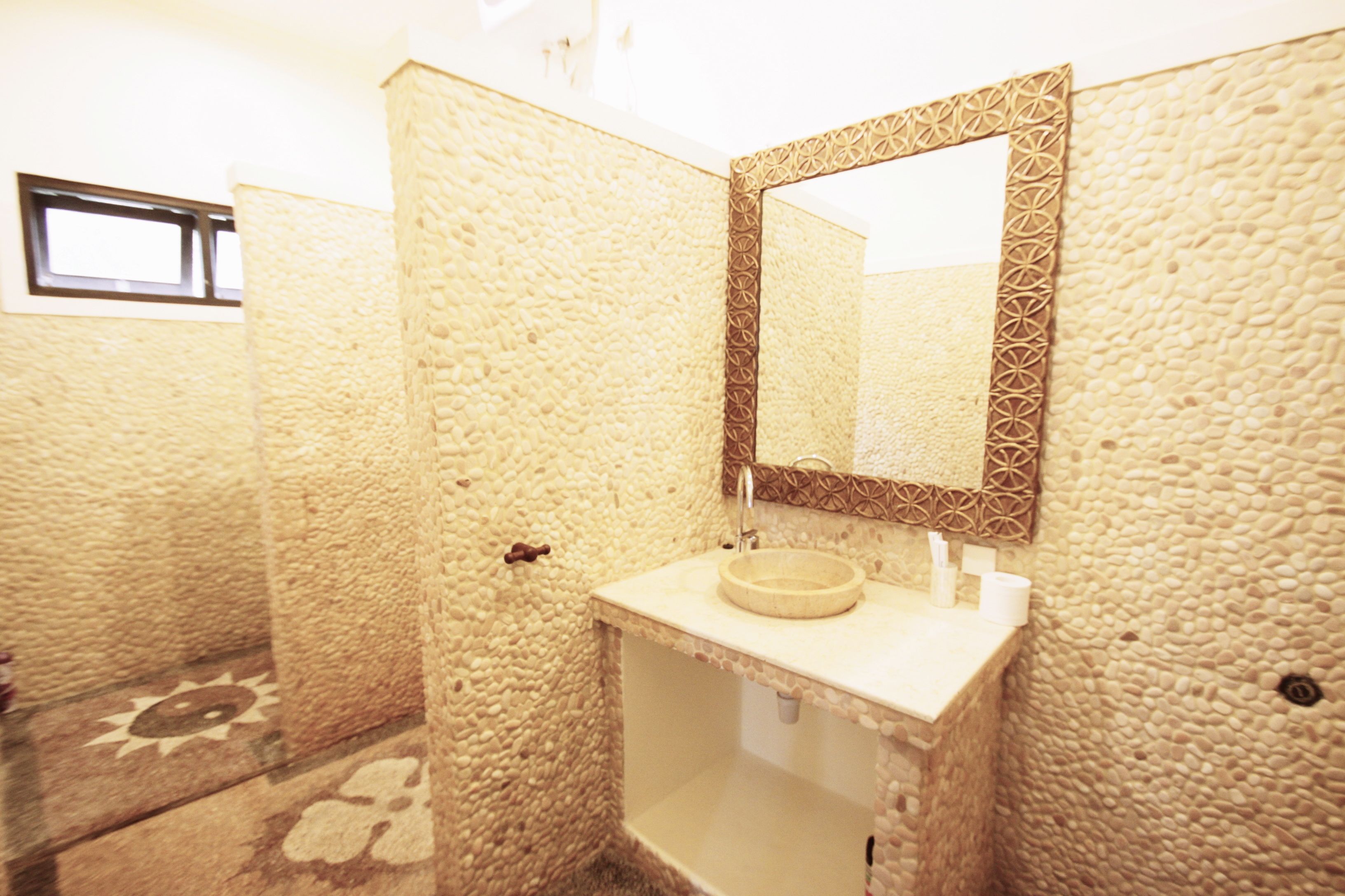 Un baño con paredes texturizadas, un lavamanos redondo y un espejo decorativo.