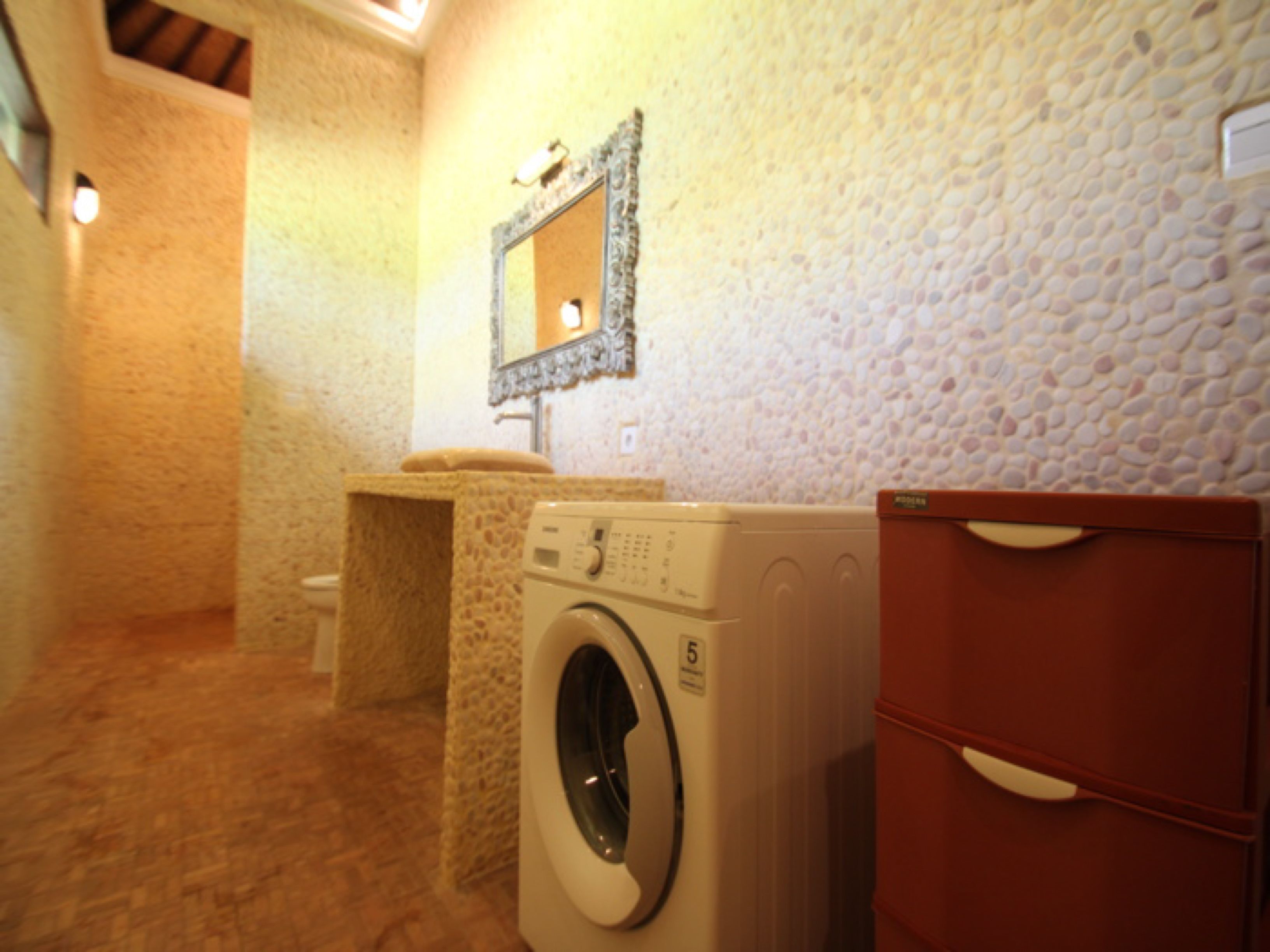 A laundry area with a washing machine, a mirror, and a wooden cabinet.