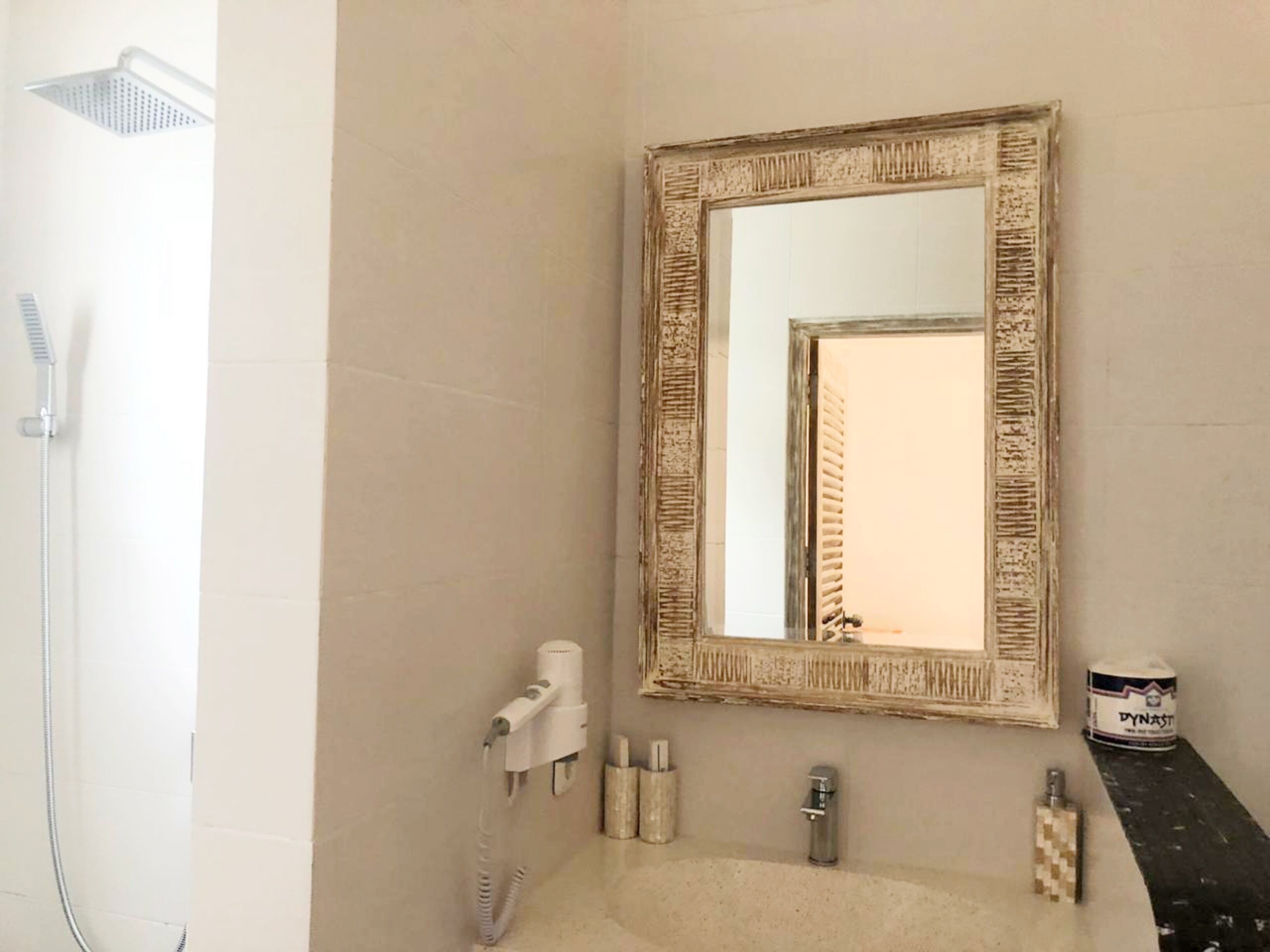 A bathroom with a shower, a sink, a mirror, and toiletries.