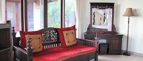 A traditional wooden bed with red and gold cushions, a wooden nightstand, a mirror, and a lamp.