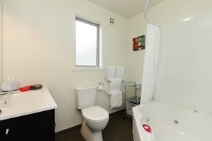 A bathroom with a white toilet, a sink with a mirror, a bathtub, and a shower curtain. - Ellena Court Motel (Blenheim)