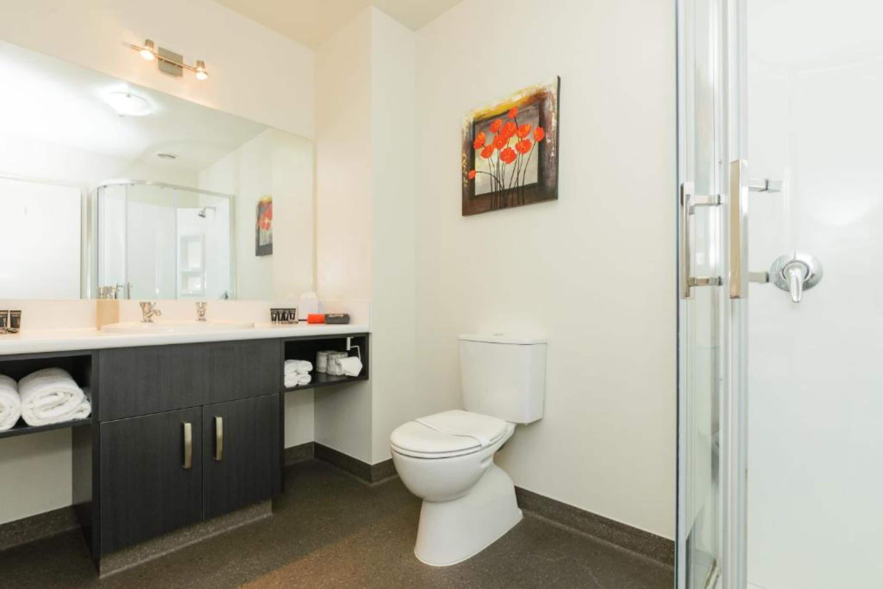 A modern bathroom with a white toilet, dark wooden cabinets, a glass shower enclosure, and a large mirror.