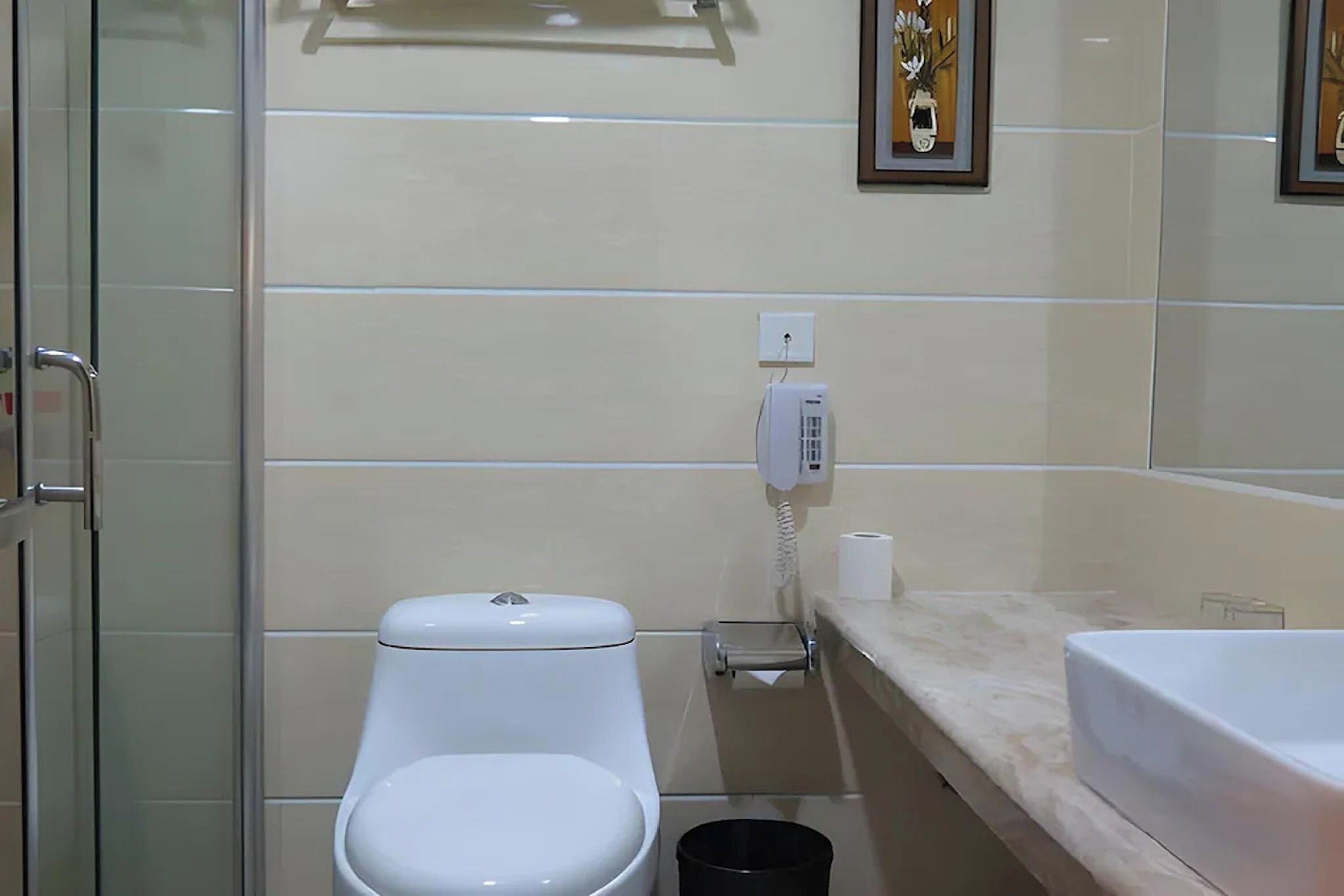 A bathroom with a toilet, a hand dryer, a trash bin, and a sink.