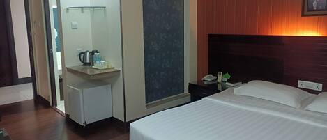 Habitación de hotel con cama, un pequeño escritorio con teléfono, un espejo y estante en la pared.