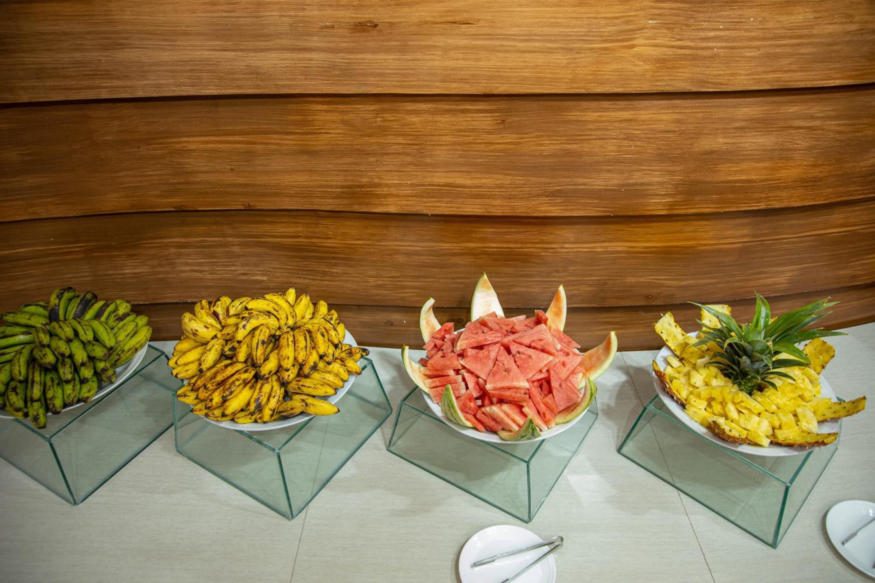Four glass display stands with different fruits: bananas, watermelon, and pineapple slices.