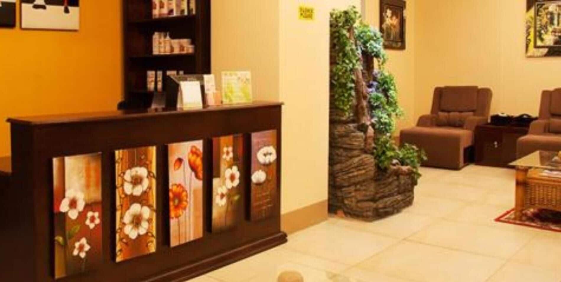 A reception area with a wooden counter displaying floral artwork, a small indoor garden, and a seating area with brown sofas.