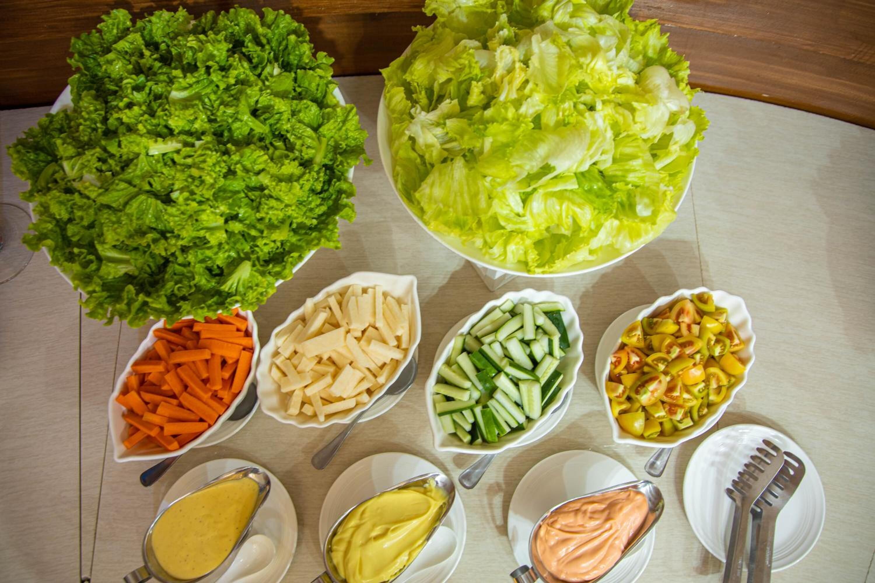 A table with various food items including lettuce, carrots, cucumbers, and cheese, along with three types of sauces.