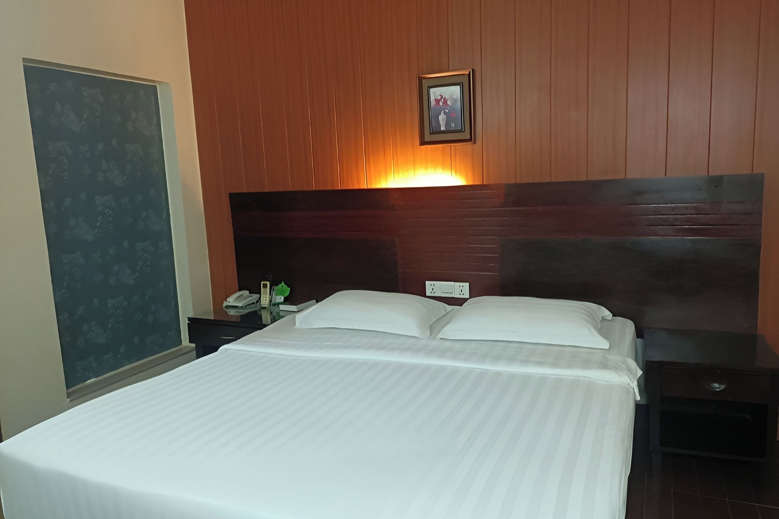 Habitación de hotel con una cama grande, una mesita de noche, un teléfono en la pared y un cuadro enmarcado sobre la cama.