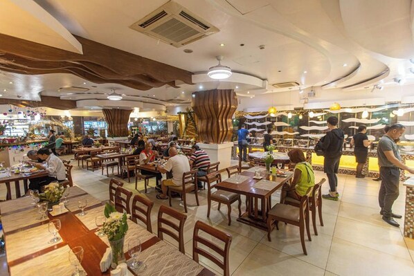 Un restaurante espacioso con varias áreas de comedor, muebles de madera y una columna decorativa central.