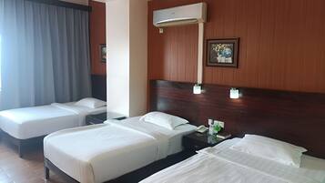 A hotel room with three beds, a wooden headboard, an air conditioning unit, a bedside table with a phone, and a framed picture on the wall.