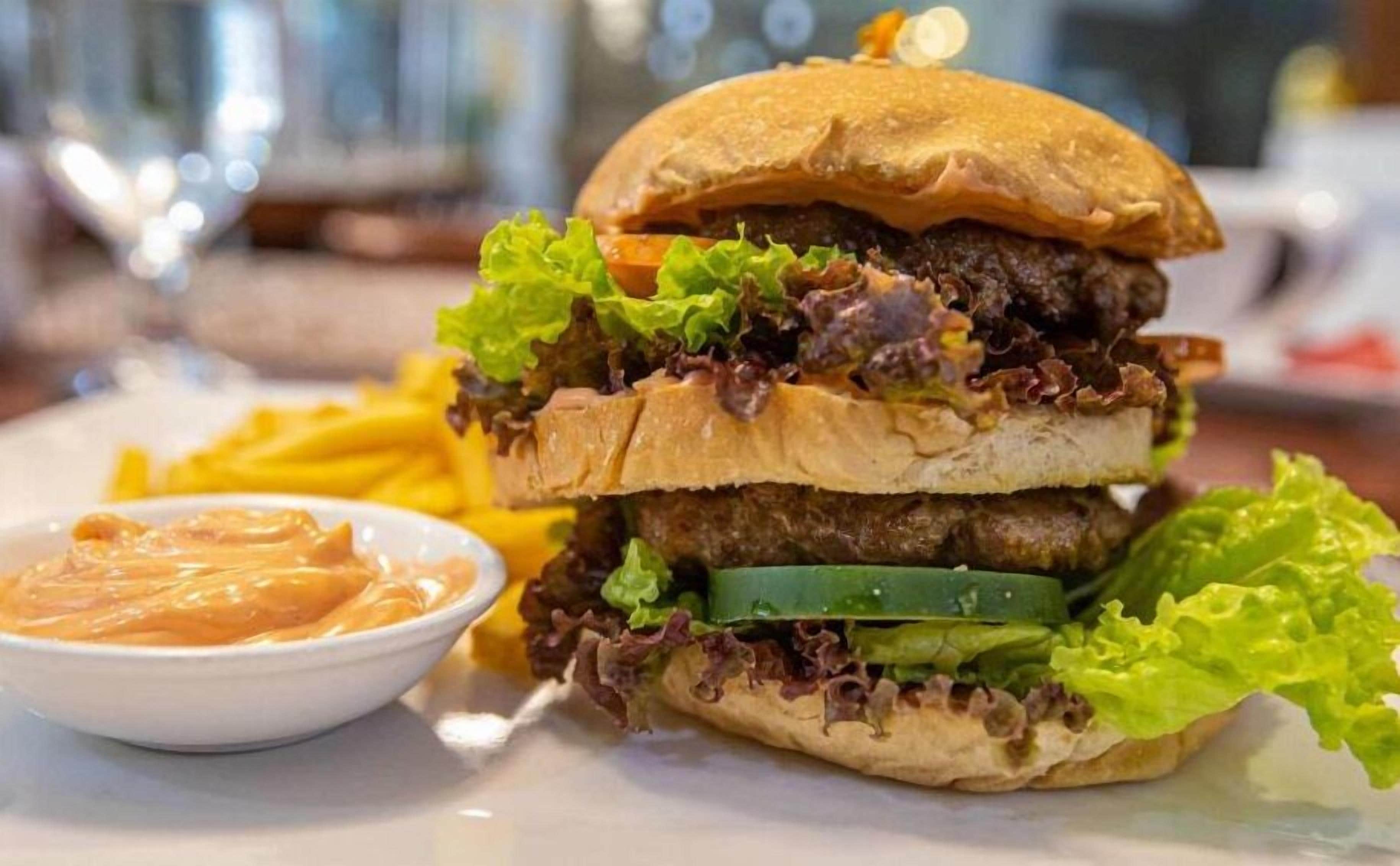 A burger with lettuce, a side of fries, and a small bowl of sauce.