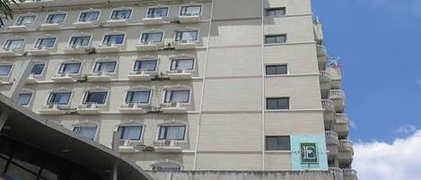 Un hotel de varios pisos con balcones, unidades de aire acondicionado y un cartel que indica un centro de negocios.