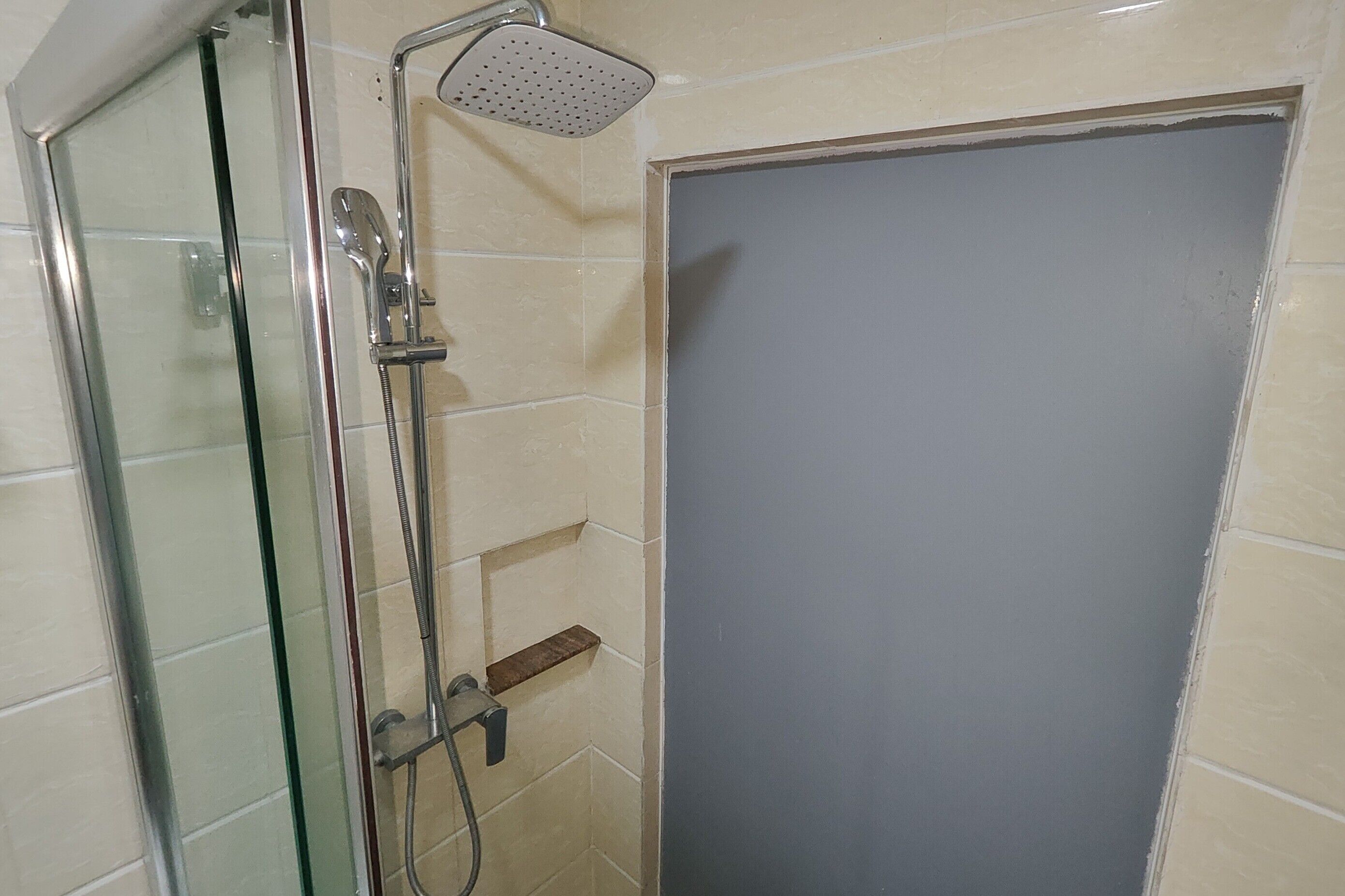 A glass-enclosed shower with a handheld showerhead and a wall-mounted faucet.