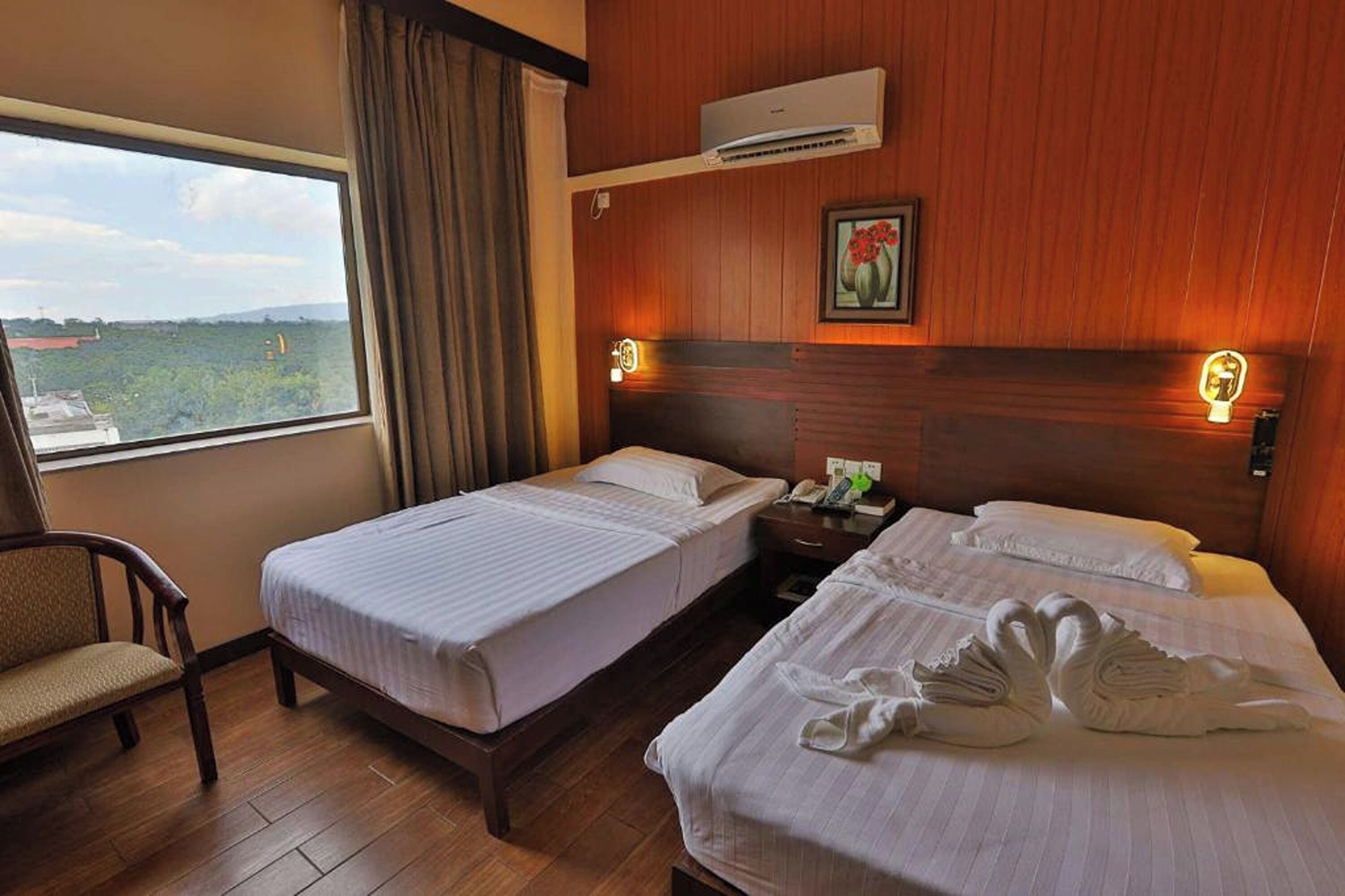 Camera d'albergo con due letti, una poltrona, una finestra con vista e un condizionatore d'aria.