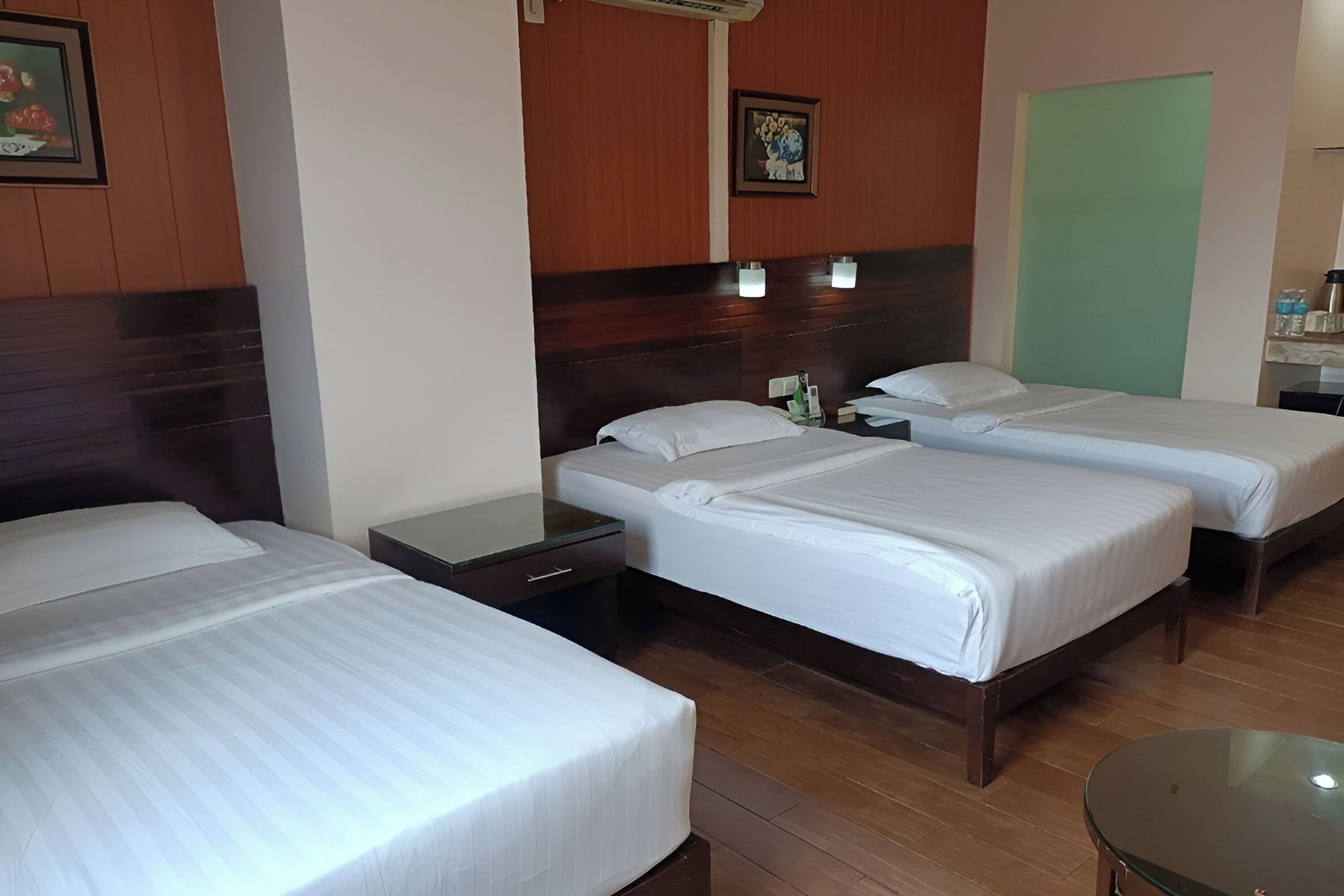 A hotel room with three beds, wooden headboards, a small table, and a green partition wall.