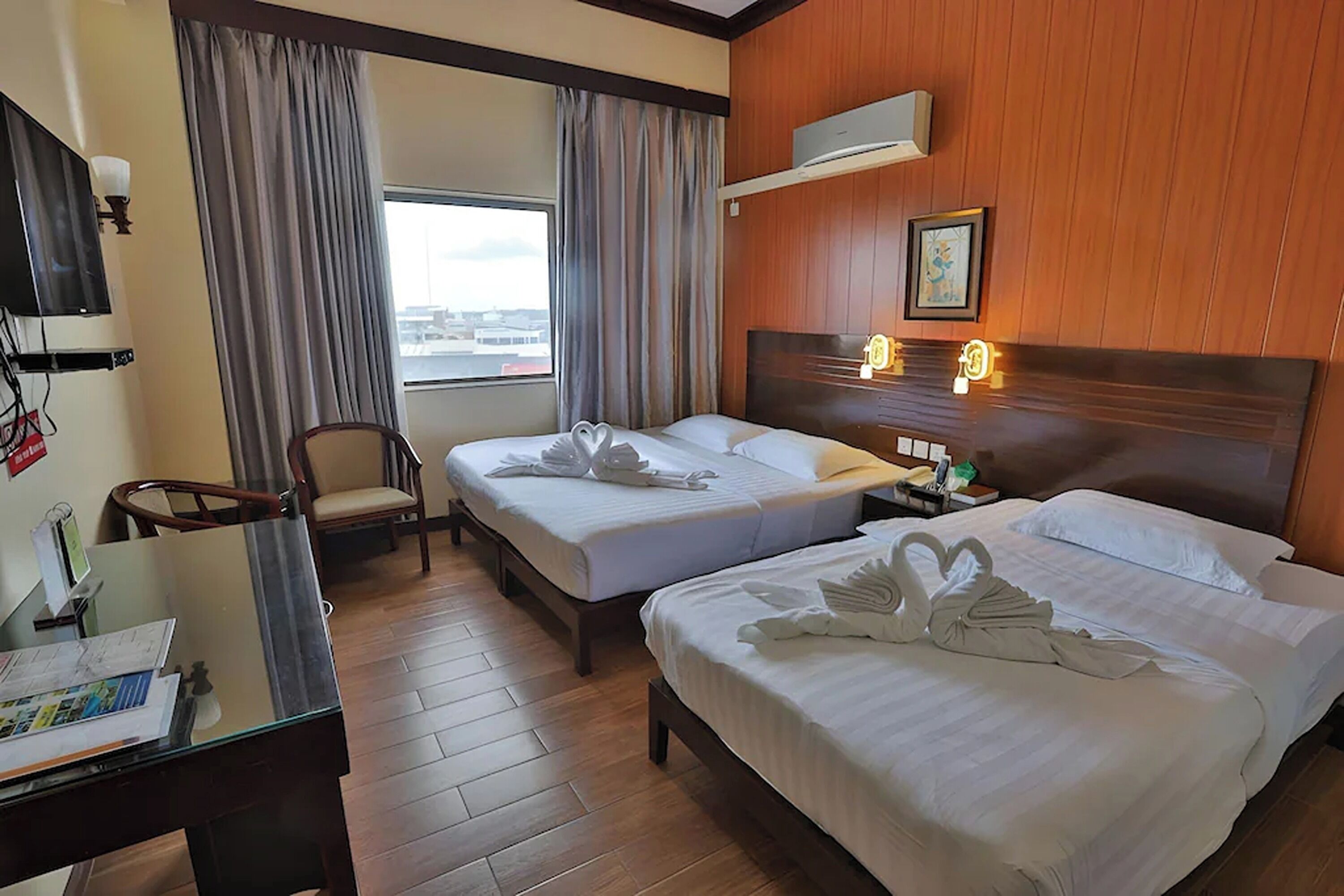 Habitación de hotel con dos camas, un escritorio, una silla, un televisor y una ventana con cortinas.