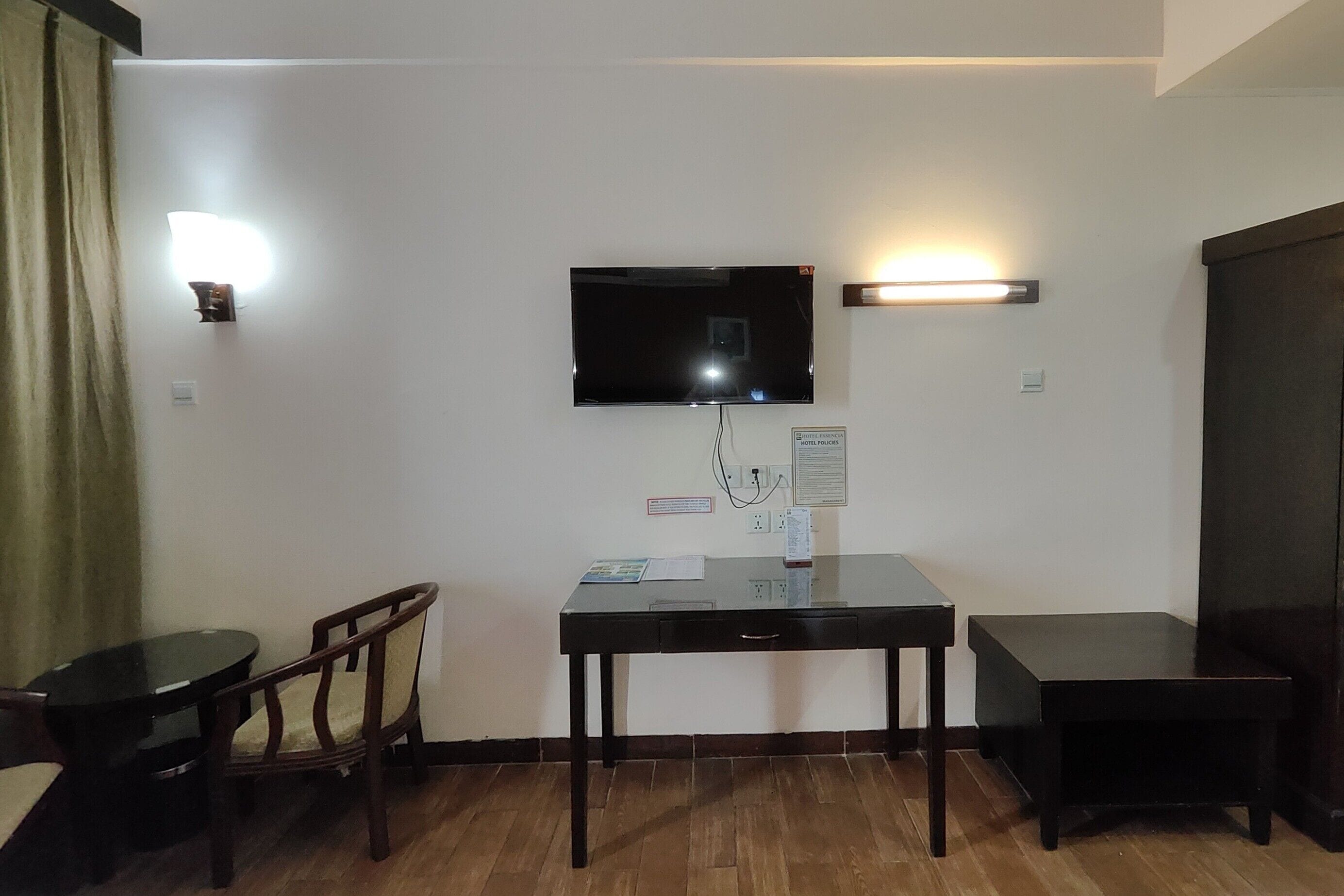 Habitación de hotel con televisión de pantalla plana en la pared, una mesita con una silla y suelo de madera.