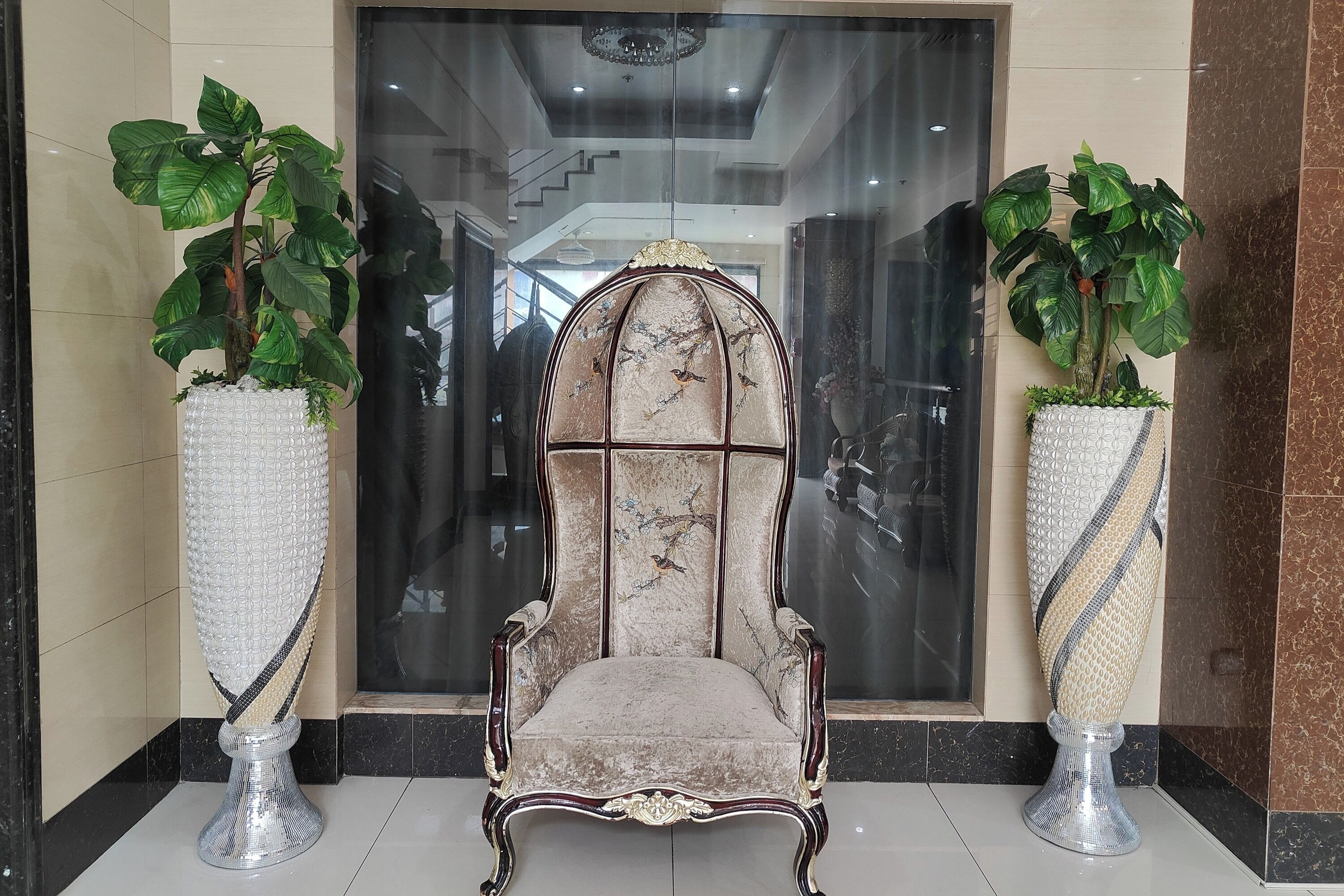 A grand chair with a marble backrest and a plush seat, flanked by two large potted plants with broad leaves.