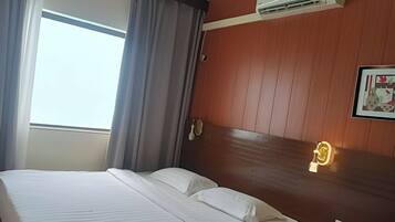 A hotel room with a bed, curtains, an air conditioning unit, a wall-mounted phone, and a light fixture.