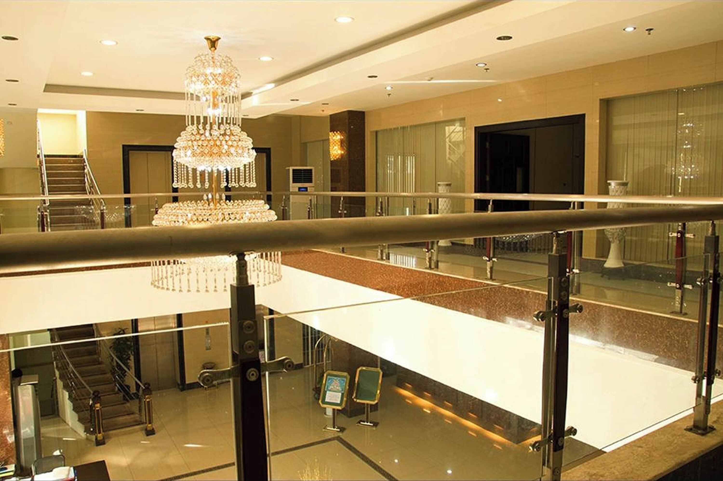 A hotel lobby with a grand chandelier, a glass railing, and a staircase leading to an upper level.