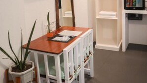 A hotel room with a wooden table, white chairs, a television, a mirror, a wardrobe, and a small plant. - 8Colors Beach House (Boracay Island)