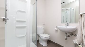 Un baño moderno con cabina de ducha de vidrio, inodoro blanco y lavamanos con espejo.