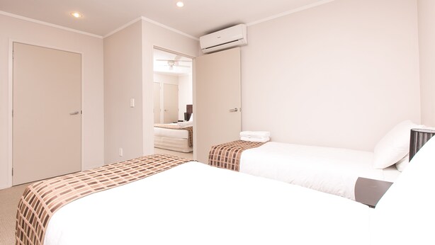 A hotel room with two beds, a wardrobe, an air conditioning unit, and a bathroom visible through an open door.