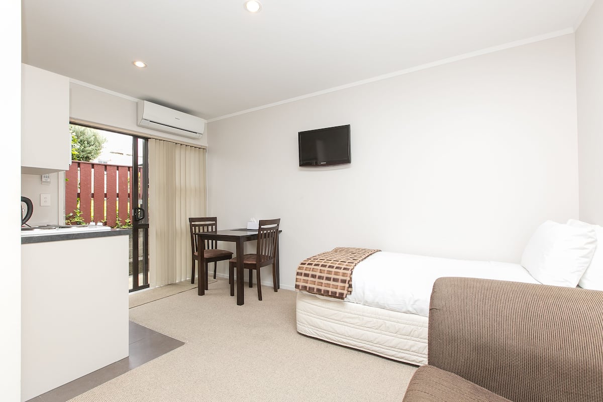 Habitación de hotel con cama, televisor montado en la pared, una pequeña mesa con sillas y un equipo de aire acondicionado.